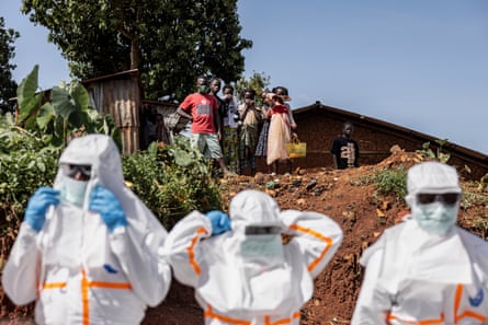 Health workers in PPE watched by members of a community prepare for a safe burial operation of people who died from Ebola