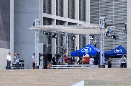 Behind-the-scenes view of the interview at the top of a set of steps with photographers and videographers in the background.
