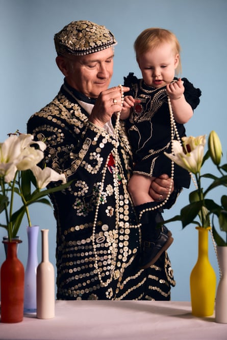 Keith Crowe, the pearly king of Homerton, holding a small child who is also wearing a pearly outfit