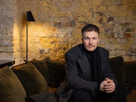 A man successful achromatic pinch a bladed moustache sits connected a sofa looking astatine nan camera