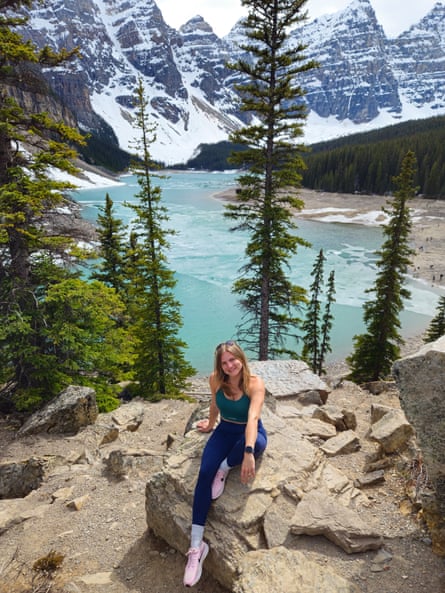 Jelena sitting on rocks with a vew of tall trees, a clear blue lake and snowy mountains behind