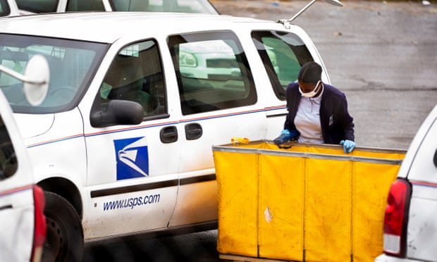 A USPS employee wearing a protective face mask loads mail into a vehicle to be delivered at a post office in Washington DC on 28 April 2020.