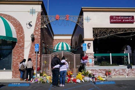 People stand in front of a makeshift memorial outside of the gates of a business.