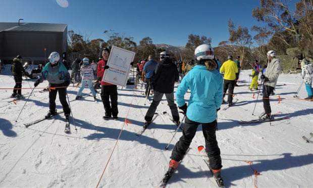 Social distancing on the slopes, an employee surrounded by skiiers at Merritts in Thredbo holds up a sign instructing people to remain 1.5m apart.