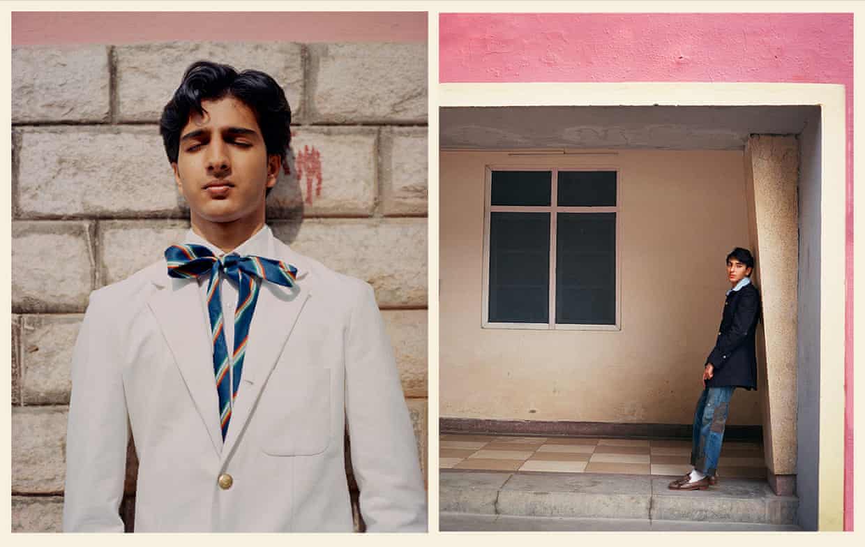 A man in white blazer and bow tie, another in a jeans and a blue blazer, leaning in a pink archway