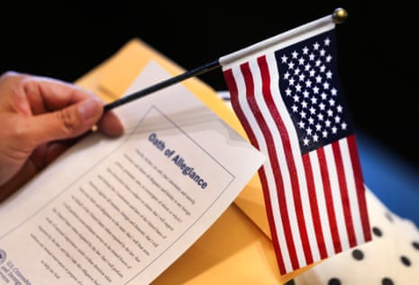 A woman holds an American flag and a printout of the oath of allegiance next to a manila envelope