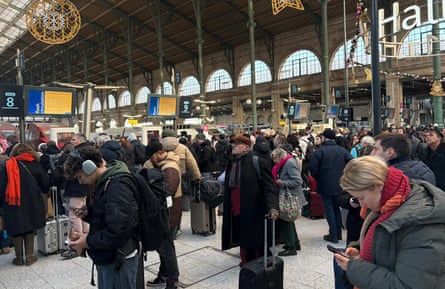 People stand in a departures with luggage, many looking at departures screens or their phones