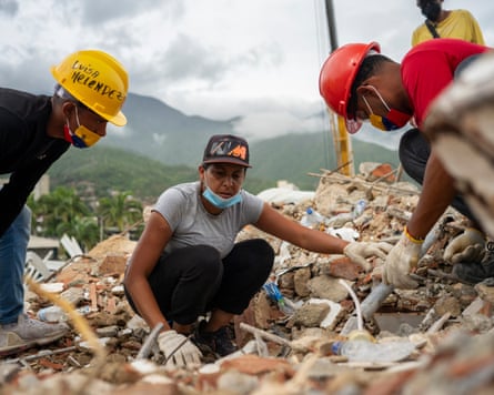 Luzmar Olivares crouches down above some rubble