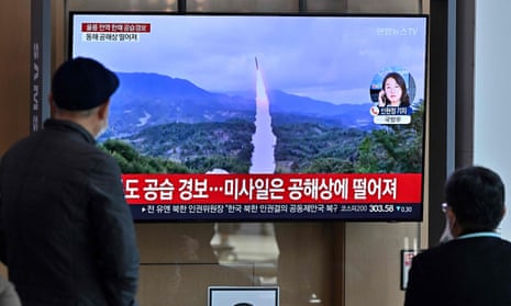 people watch a television screen showing file footage of a North Korean missile test