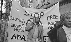 Black-and-white photo of man standing in front people holding a protest sign
