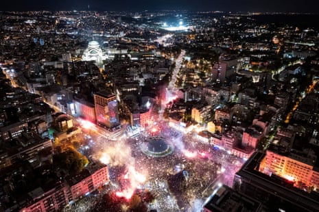 Aerial night view of a huge crowd filling Belgrade’s Slavija Square, with flares and smoke rising