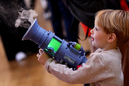A young boy holds a blue plastic space gun with smoke coming out of the barrel