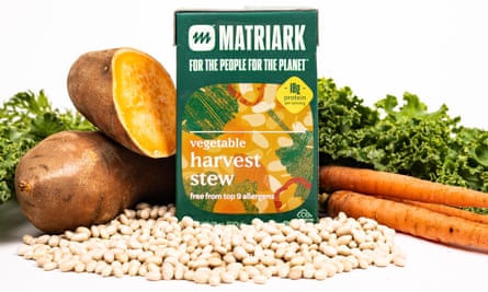 Stock image of a green and orange bags of “organic harvest stew”, surrounded by a pile of beans, sweet potatoes, and carrots.