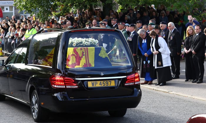 People bow their heads in respect as the coffin of Queen Elizabeth II passes through the village of Ballater.