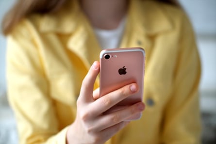 A teen in a yellow top holds an iPhone in her hand.