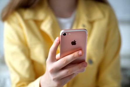 A teen in a yellow top holds an iPhone in her hand.