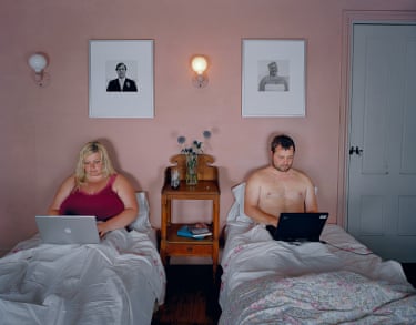 Jesse, Kerry, 2005. Years before it became a public anxiety, Del Amo pictured how technology contributes to isolation even in shared space. In this photograph a young couple is side by side in separate beds, each staring at a laptop, their faces illuminated by the screens. The wedding portraits of her over his bed and his over hers suggest the novelty of their matrimonial status, yet there is already a lack of affection.