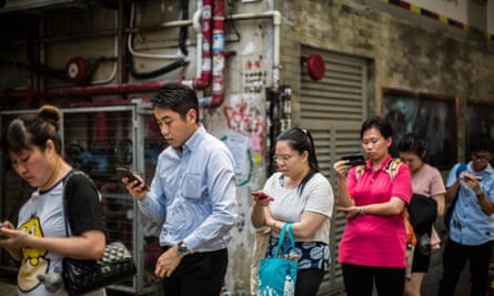Hong Kong commuters look at their mobile phones as they wait in line for a bus.