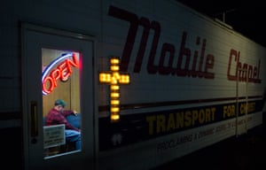 Truck driver Ben Blackburn, 46, participates in a Bible study session at the Transport For Christ mobile chapel in Lodi. An illuminated cross is on the outside of the vehicle. A fluorescent sign is pictured above Blackburn's head; it reads 'Open'.