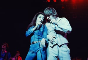 A man and woman sing into microphones on stage