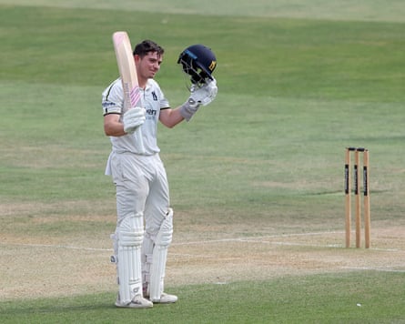 Ethan Bamber raises his bat in celebration after he reaches his century for Warwickshire against Essex.