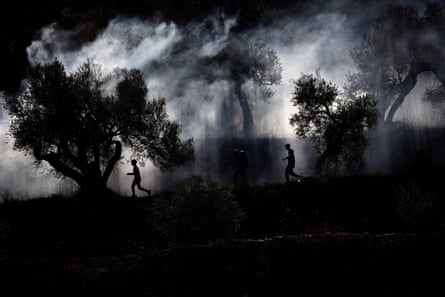 Three people, silhouetted, running amid trees, smoke and shadows
