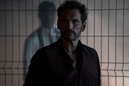 person wearing black button-down, with silhouette of person in screen door in the back