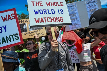 A person in a crowd of other protesters holds a sign that reads ‘the whole world is watching’.