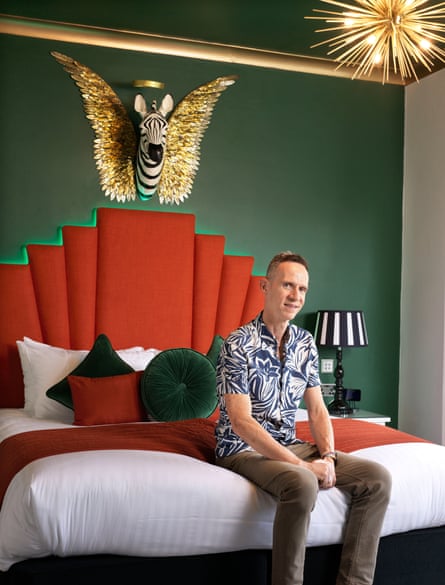 Julian Banner-Price sits on a bed in an ornate hotel room