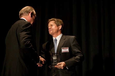 Two men wearing black suits shake hands on stage