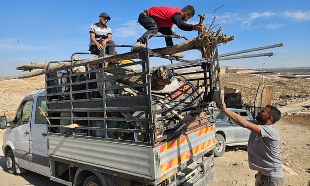 A man secures a long piece of wood on a pickup truck as another holds the door at the back