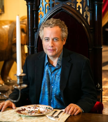 Chris Mark sitting at a grand table in an ornate high-back chair with a candlestick to his right and a plate and cutlery on the table in front of him