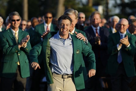A crowd of men in green jackets applaud as Rory McIlroy puts on his green jacket during the winner’s ceremony
