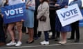 A small group of men and women, some wearing blue are seen from the shoulders down; two carry placards saying Vote Conservative