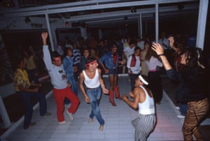 People dancing on a dancefloor. Two men in the centre are wearing vest tops and headbands, while another wears a Mickey Mouse jumper and red trousers