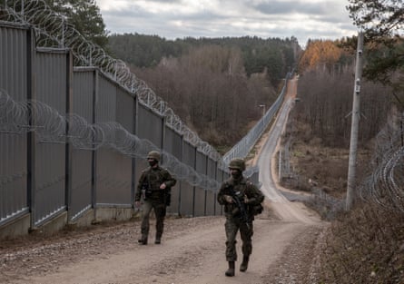 Two soldiers walking along a path by a barbed wire fence