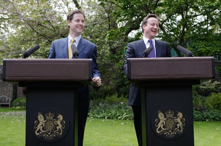 Nick Clegg and David Cameron, both wearing navy suits and standing at lecterns in a garden