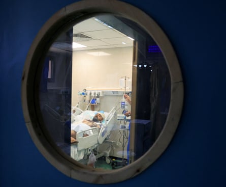 Hamdi Al-Najjar seen through the window of a door lying in a hospital bed