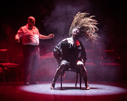A seated woman in tattered dark costume whips her hair as a man gestures nearby, in Blackout.