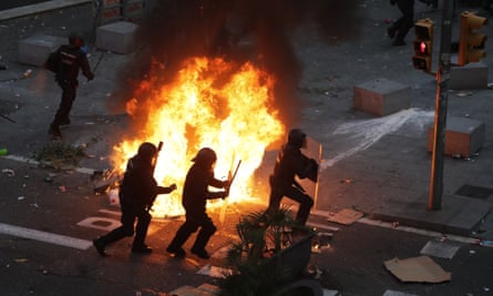 Riot police officers run past a burning barricade in Barcelona.