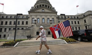 Don Hartness carries the Mississippi state flag and the American flag in front of the Capitol building.