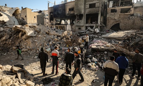 people walk between destroyed buildings