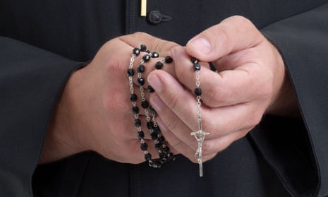 Priest's hands holding cross and rosary beads