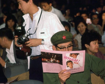 A man in a green official-looking Chinese uniform reading a leaflet about a Wham! concert