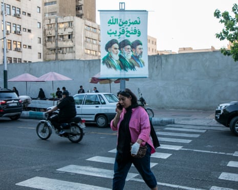 A pedestrian walks beneath of poster of the current and former supreme leaders of Iran in Tehran on Thursday