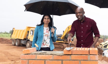 Braverman and Nsabimana lay bricks standing under umbrellas with construction lorries behind them