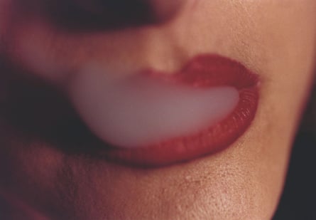 A closeup of a woman's red-painted mouth with smoke wafting out of it
