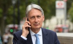 Philip Hammond holds a mobile phone to his ear while walking along a street