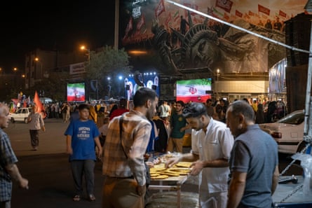 People buy bread from a sidewalk vendor beneath an anti-US billboard