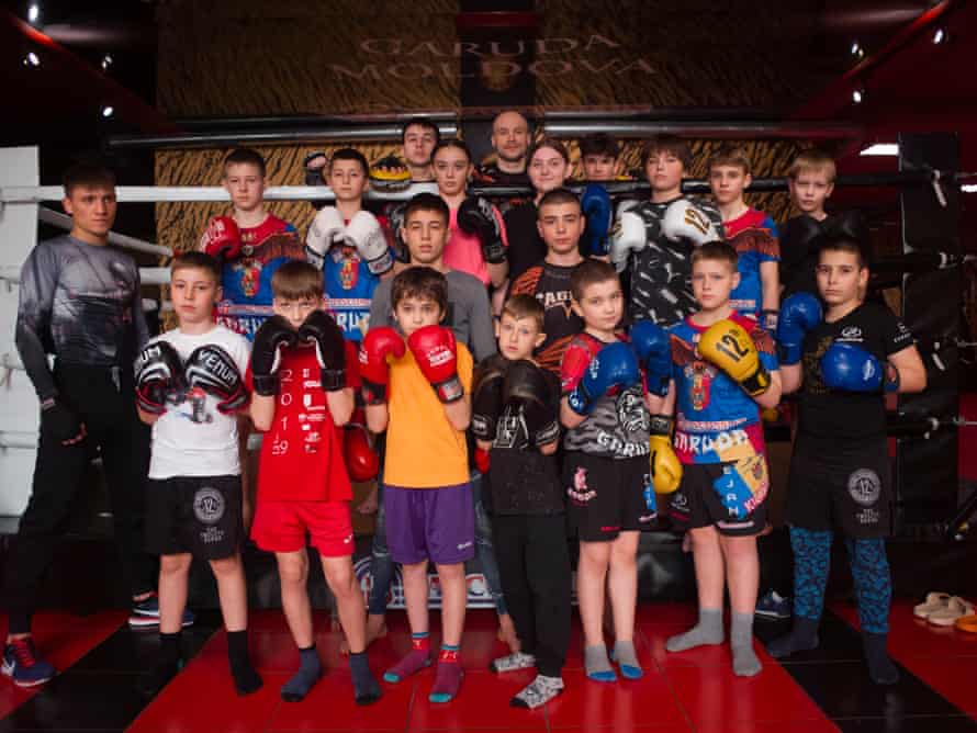 A group of boys and girls with boxing gloves on and fists up pose in a boxing ring